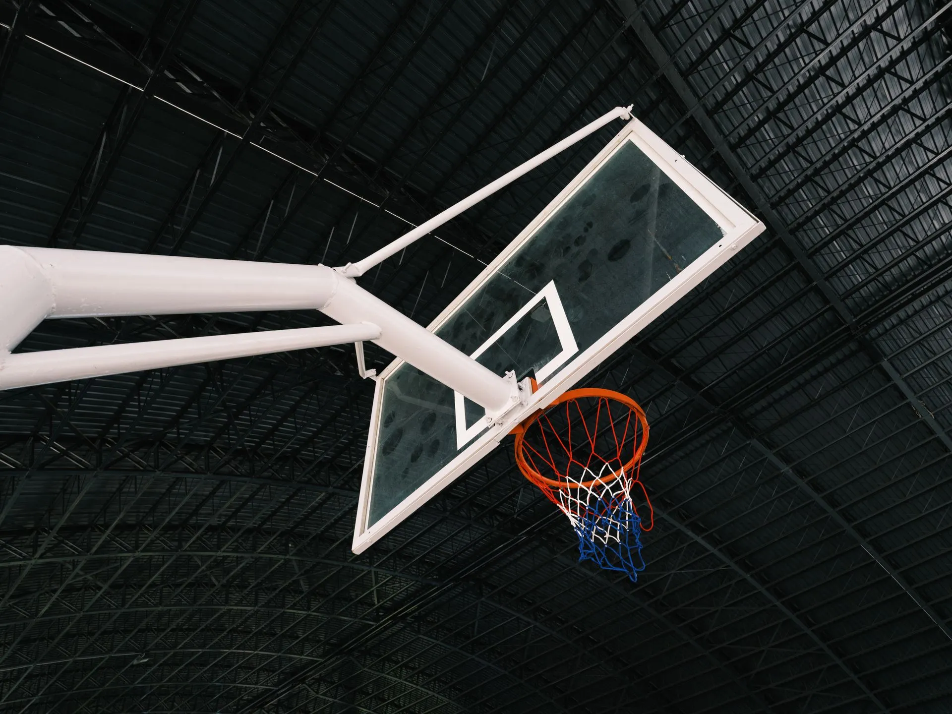 Indoor basketball backboard with white metal support arms, orange rim and net